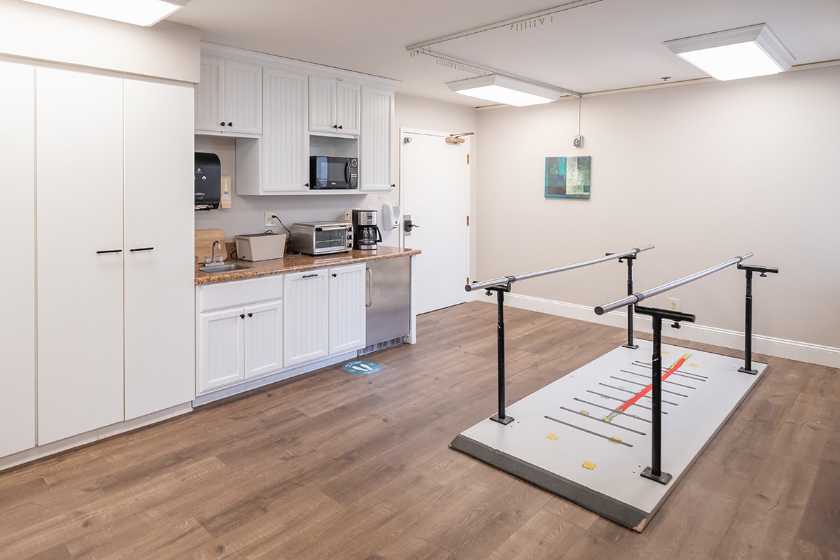Rehab gym with parallel bars and kitchenette at Arbor Post-Acute